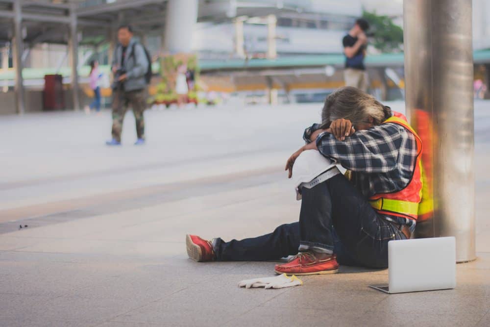 Tired worker sitting on the ground with head down, highlighting workplace fatigue management.