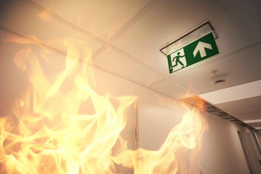 Flames in a hallway near an emergency exit sign, emphasizing fire safety and evacuation training.