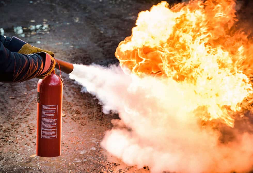 Person using a fire extinguisher to put out flames, highlighting fire safety training.