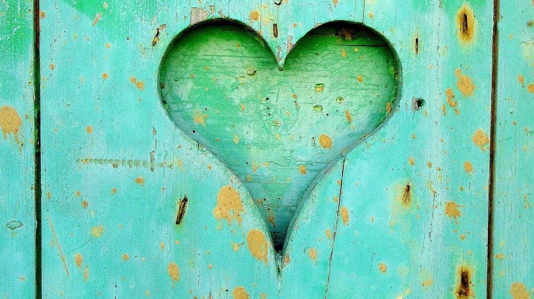 Heart-shaped cutout on a weathered turquoise wooden surface, symbolizing care and wellness.