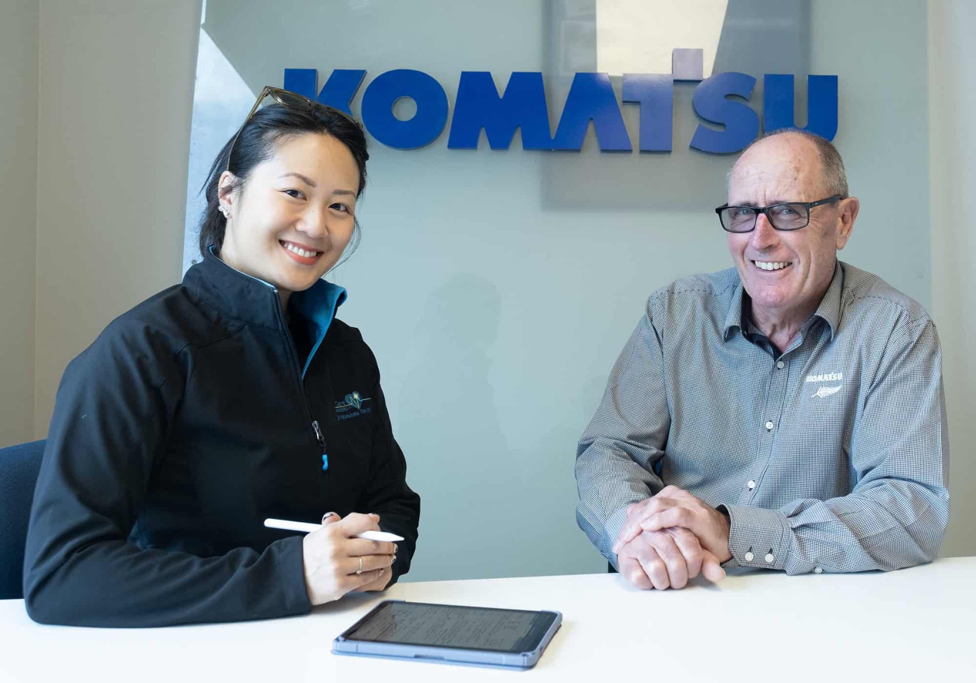 Two Komatsu employees smiling during a meeting, highlighting collaboration with Life Care.