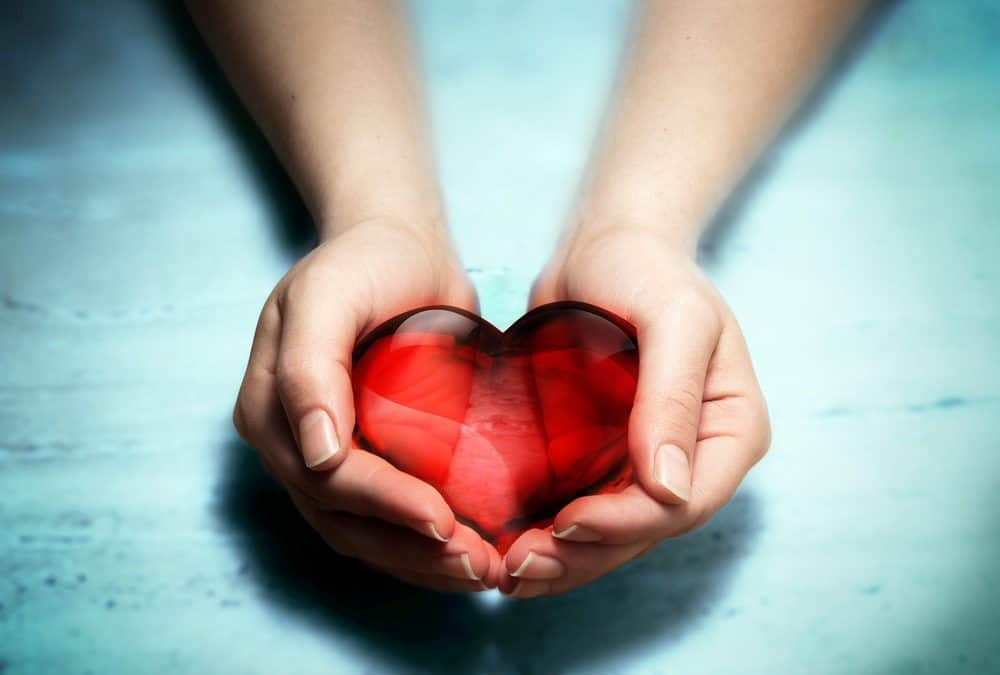 Hands gently holding a red glass heart, symbolizing care and compassion.