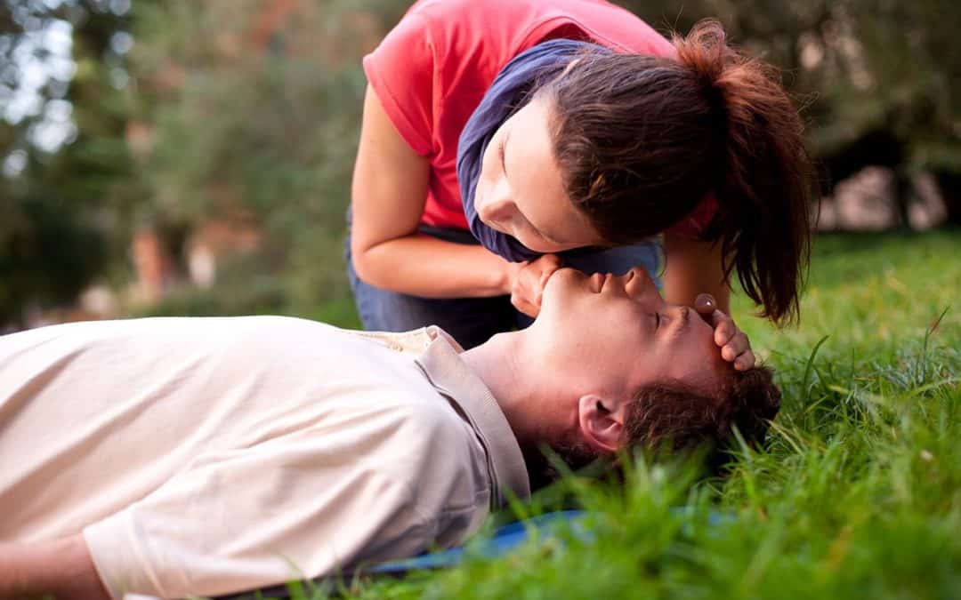 Woman performing CPR on an unconscious man during a first aid training session outdoors.