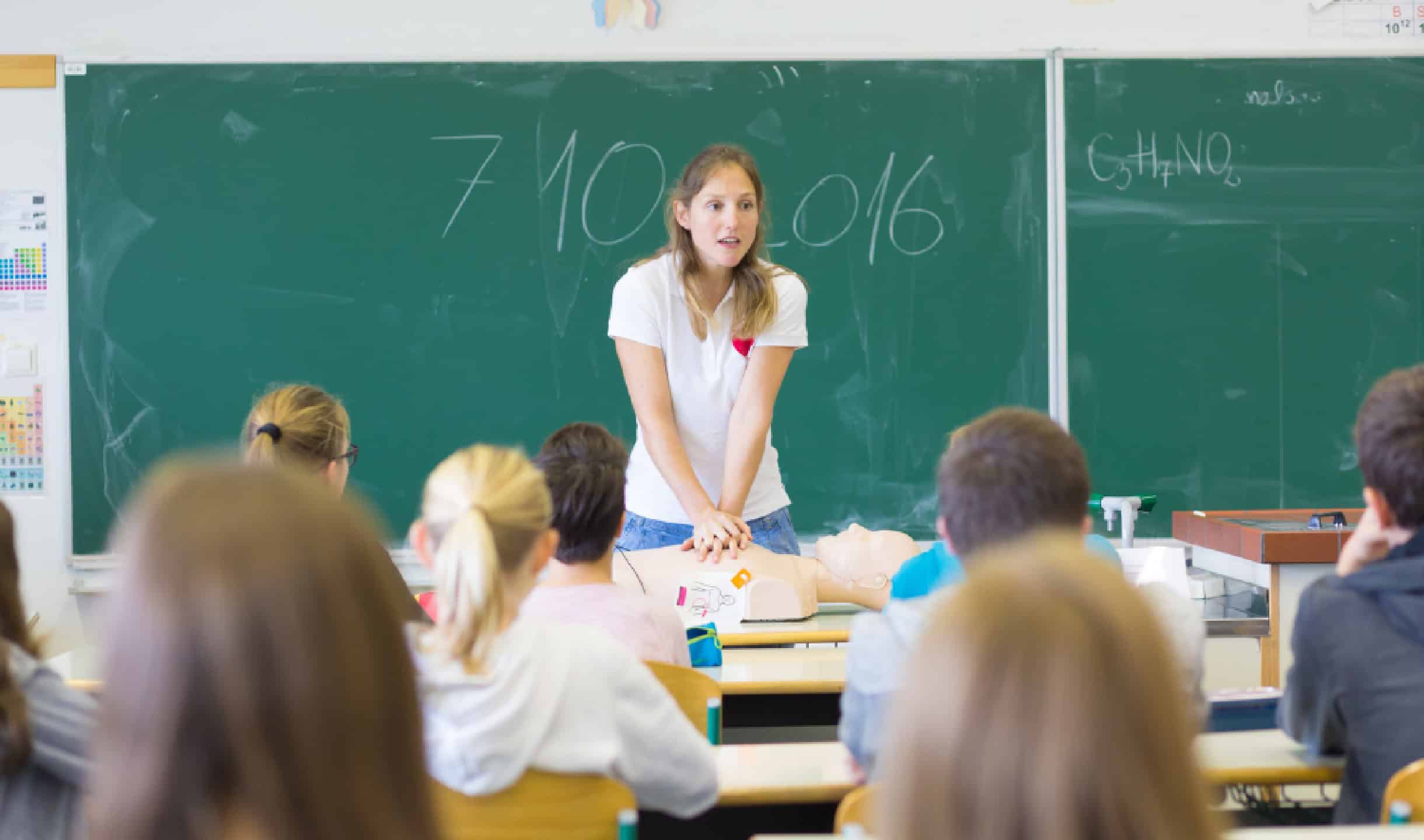 Instructor demonstrating CPR techniques to students in a classroom setting.