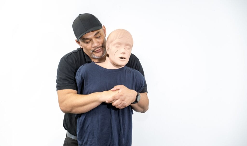 Instructor demonstrating the Heimlich maneuver on a CPR training mannequin.