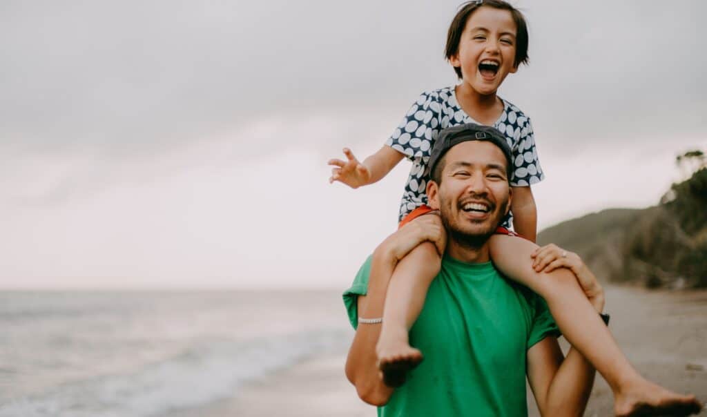 Smiling father carrying a joyful child on his shoulders while walking on the beach