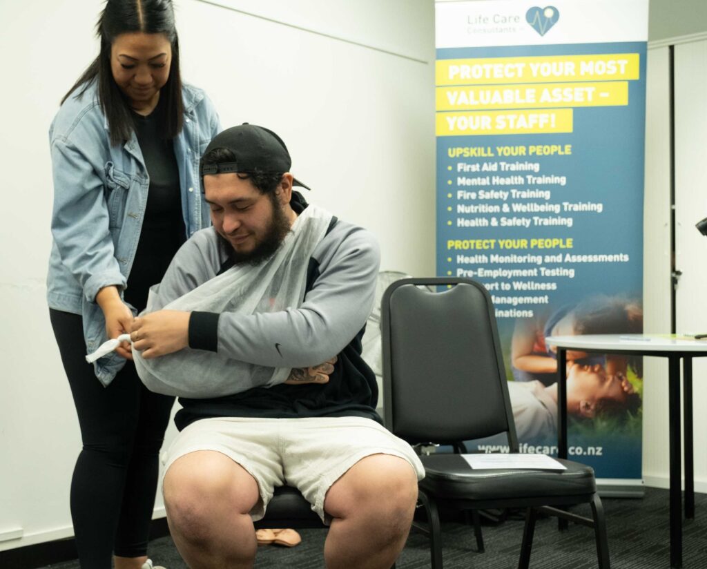 First aid training participant receiving guidance on how to apply an arm sling during class.