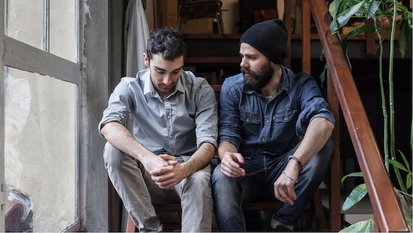 Two men sitting together, one offering emotional support to the other.