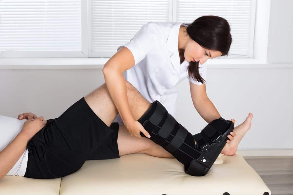 Physiotherapist adjusting a medical boot on a patient's leg during treatment.