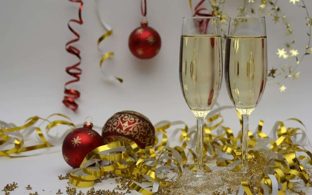 Two champagne glasses with festive decorations, red ornaments, and golden ribbons.